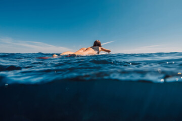 Surf girl rowing on surfboard. Woman in ocean and sunny day