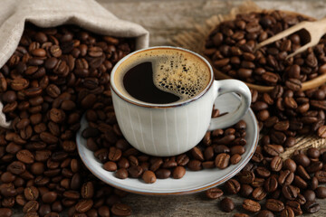 Cup of aromatic hot coffee and beans on wooden table