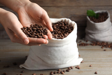 Woman taking roasted coffee beans from bag at wooden table, closeup. Space for text