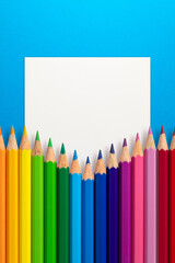 Creative layout made of color pencils on blue paper background with white paper card note. Flat lay. Education concept.