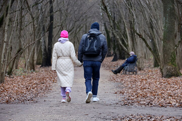 Couple walking in autumn park. Man and girl holding hands, concept of relationship, romantic date at cold weather