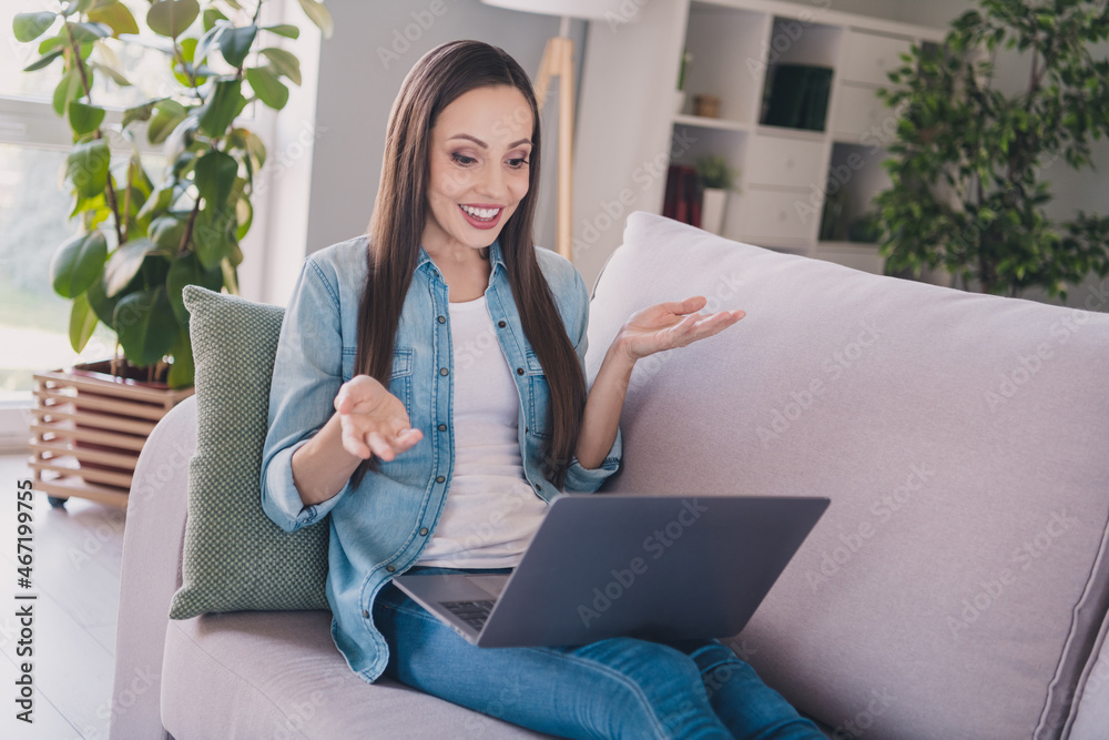 Sticker Portrait of attractive cheery long-haired woman sitting on divan using laptop calling on web friend at home indoors