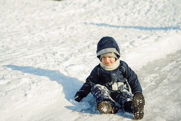 cute caucasian boy sliding down the icy slope in park . Winter activities concept. Happy childhood.