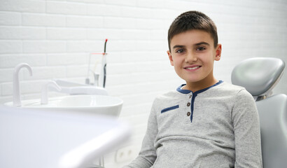 Adorable child preadolescent boy sitting in dentist's chair during dental appointment for regular...