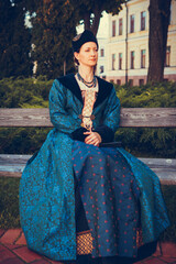 Fototapeta premium Portrait of woman dressed in blue historical Baroque clothes with old fashion hairstyle, outdoors. Luxurious medieval dress