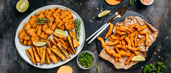 Assortment of baked sweet potatoes with cfries with lime and herbs on plate, on dark background. Long banner format. top view