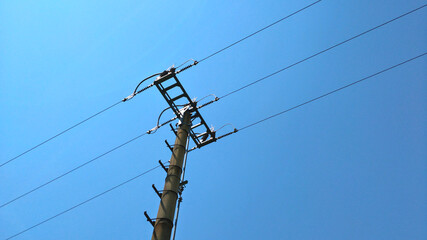 Detail of top part of low voltage pole of local electrical grid seen against blue sky. There are...