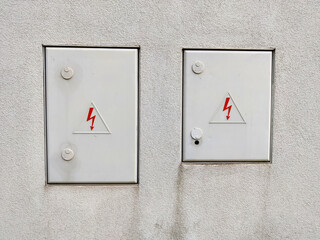 White wall with two doors for electrical distribution grid maintenance entrance. Both doors have symbol of red lightening on it.