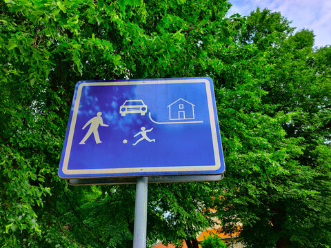 Traffic sign showing that the area is residential so cars should drive carefully. The background of the sign is blue with white drawing of man and children playing on the street with cars coming to th