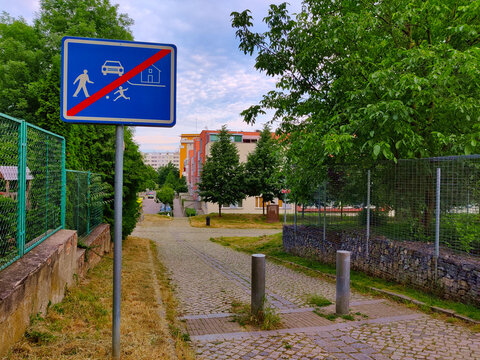 Narrow sidewalk with anti-car barrier and road sign of crossed public space. The sign tells cars that the area where people walk freely has ended. There is a fence on both sides of the road.