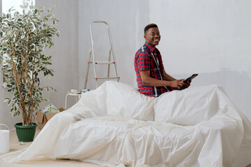 Satisfied man with dark complexion is sitting on backrest of sofa leaning against protective film...