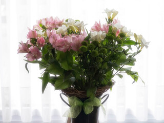 Bouquet flowers backlit in front of window with drapes