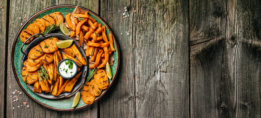 Set of homemade baked orange sweet potato fries with lime and herbs on plate. Long banner format. top view