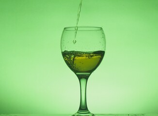 A drink (juice, cocktail, wine) is poured into a glass glass. Photo on a green background.