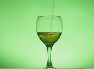 A drink (juice, cocktail, wine) is poured into a glass glass. Photo on a green background.