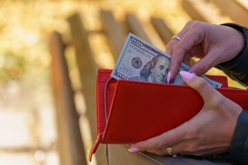 A womans hand pulls a hundred dollar bill out of her wallet. Background with copy space for text