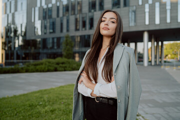 Portrait of attractive brunette businesswoman secretary in daily makeup woman wearing white shirt with jacket thrown over back cold morning evening outside in front of glass corporate office building