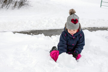 Small child, playing with snow on snowy cold winter day. Little kid making snowman. Girl wearing snowsuit, having fun outdoors.