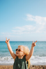 Child girl walking on beach sea outdoor baby in sunglasses 3 years old kid raised hands family fun vacations