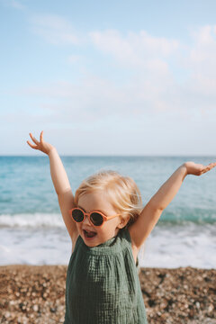 Happy child girl playing on beach emotional toddler in sunglasses 3 years old kid raised hands family travel lifestyle vacations outdoor