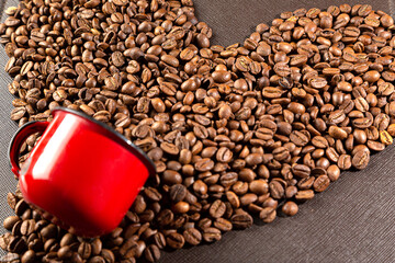 xícara de café vermelho em cima de um punhado de grãos de café torrados, que têm a forma de um...