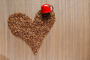 uma xícara de café de ferro vermelho derramando os grãos de café torrados, que juntos fazem a forma de um coração, sobre um fundo de madeira