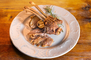 Baked lamb chops with potatoes and rosemary in white plate on rustic wooden table, warm light, top view