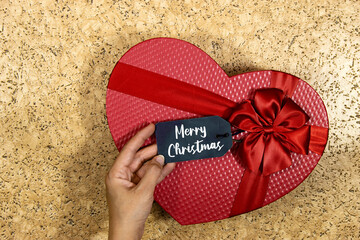 red heart shape box for holidays and hand holding a tag with merry christmas