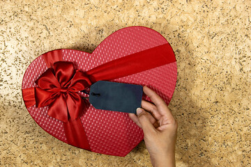 red heart shape box for holidays and hand holding a empty tag 