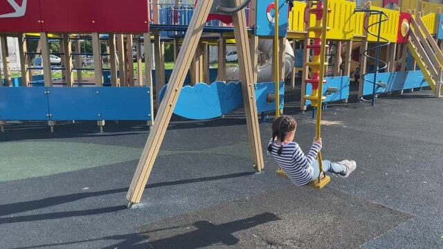 Kid riding a swing on colorful playground. 5 years old girl has fun at summer.