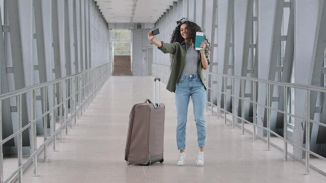 Happy Girl Woman Passenger Stands At Airport With Suitcase Holding Plane Ticket In Hand Shoots Online Video Blog Vlog Conference Call Jumps Showing Passport Into Cell Phone Camera Rejoices Trip Travel