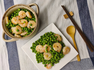 Two portions of shrimp with pea decorated on the white table cloth. One portion is in the pot and another one is on the plate.