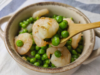 Shrimp with pea put into the beige pot with wooden spoon holding a bit of shrimp with peas.