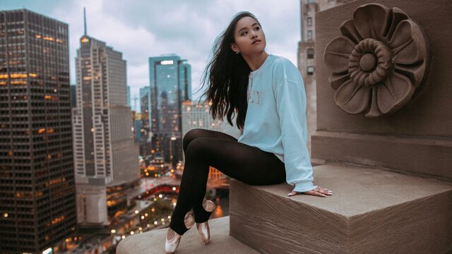 Ballerina sitting on cornice over cityscape