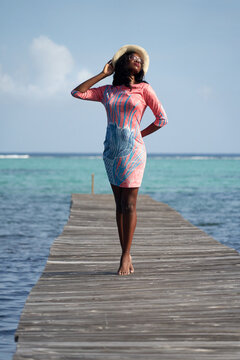 Barefooted woman in pink dress standing on wooden dock by seashore