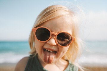 Child sticking out tongue emotional girl in sunglasses 3 years old baby walking on beach family...
