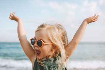 Child playing outdoor emotional surprised emotional funny girl in sunglasses 3 years old toddler raised hands family vacations outdoor - obrazy, fototapety, plakaty