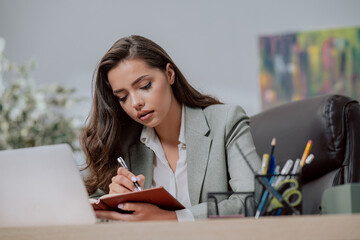 Busy, focused pretty brunette office worker, secretary, businesswoman, fulfills her duties, writes appointments in the calendar, makes notes of important information, serious face