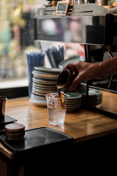 Cropped hand pouring coffee in plastic cup with ice cubes