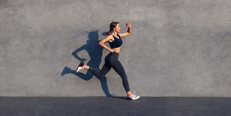 Fototapeta na wymiar Young sportive woman jumping and running on gray background, female model in sportswear exercising outdoors