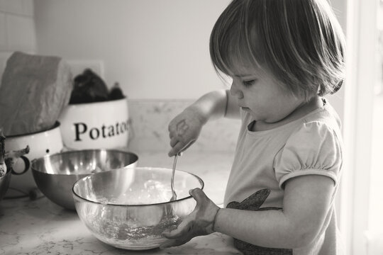 Grayscale photo of child mixing food in a bowl