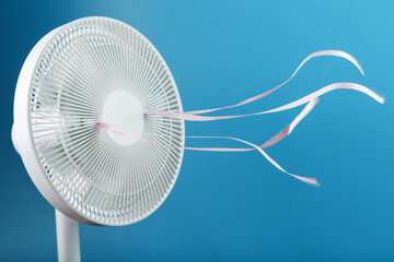 The electric fan is white with pink ribbons fluttering in the wind on a blue background
