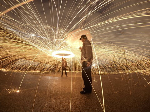 Long shot of a person making circular motion with light while another person holding an umbrella