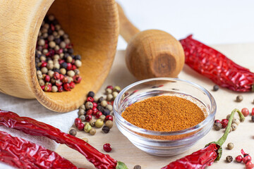 Dried peppercorn mix in the mortar with pestle, dry chili pepper powder for cooking on light wooden cutting board background in the kitchen.