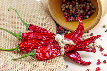 Mix of dried peppercorns in the wooden mortar and dry chili pepper for cooking on light background in the kitchen.