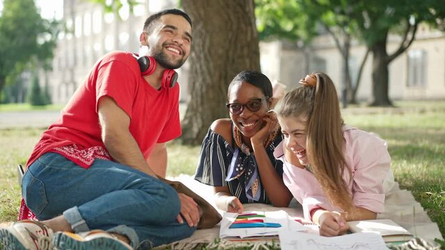 Group of young multiracial students studying talking and laughing on sunny university yard outdoors. Happy confident multiethnic men and women enjoying friendship and education. Slow motion