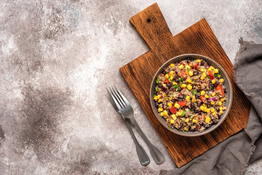 Mexican black beans corn quinoa salad in a bowl on a wooden cutting board. Rustic brown background. Top view.