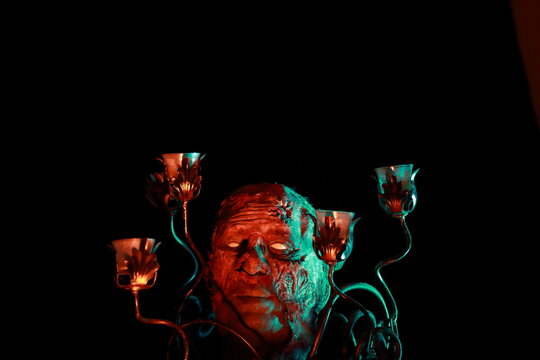 Scary face beside candle holders against dark background