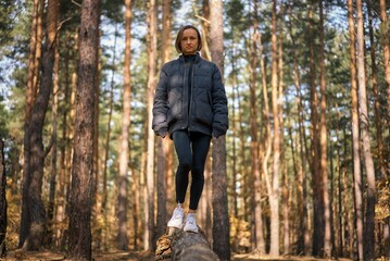 A girl walks on a log in a pine forest in autumn. Girl balancing on a log in the forest.