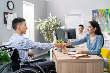 Man sits in wheelchair at desk in an office, opposite him beautiful woman in dress asks questions,...
